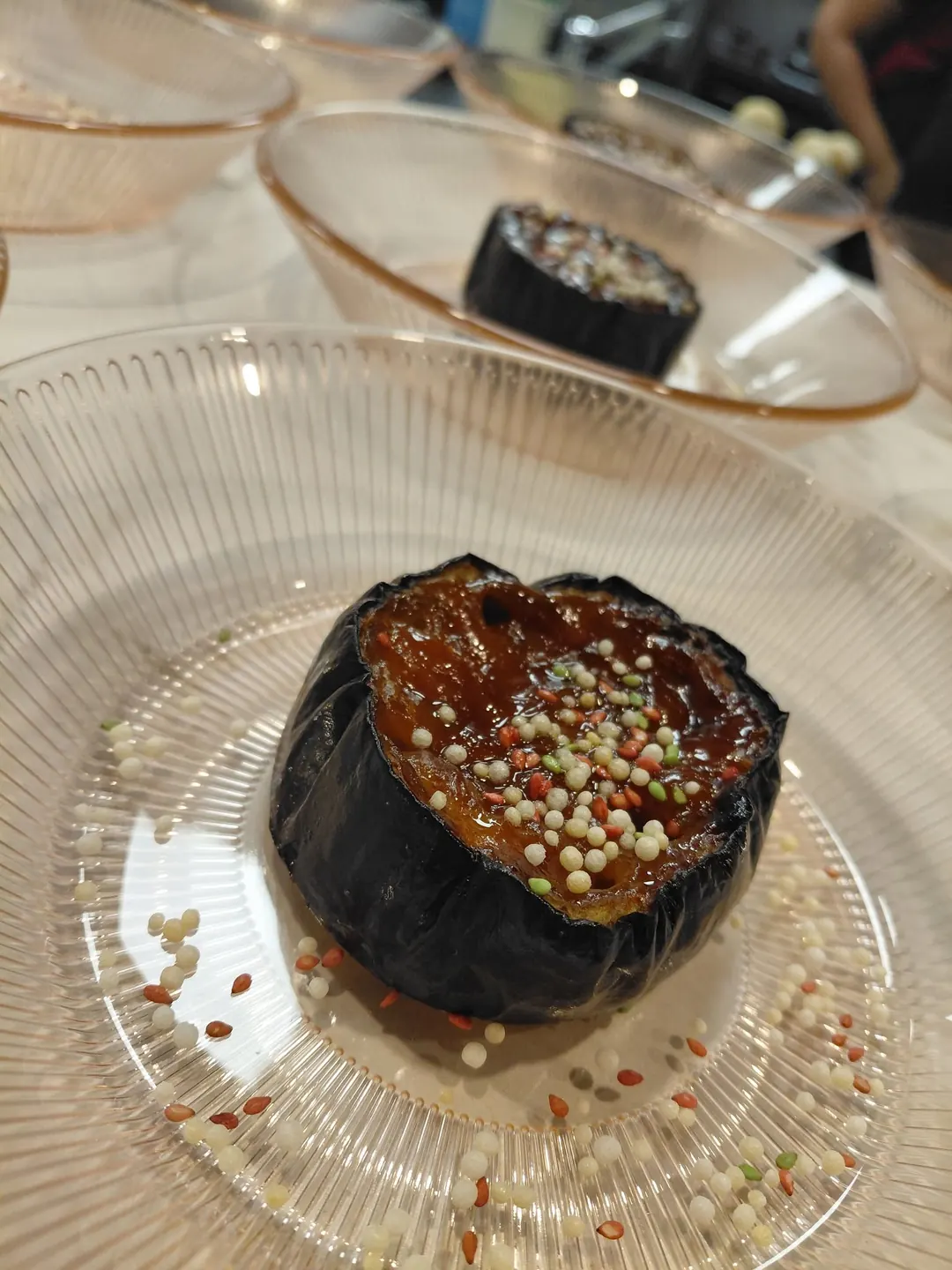 Roasted aubergine glazed and topped with pearls, on a ribbed glass plate