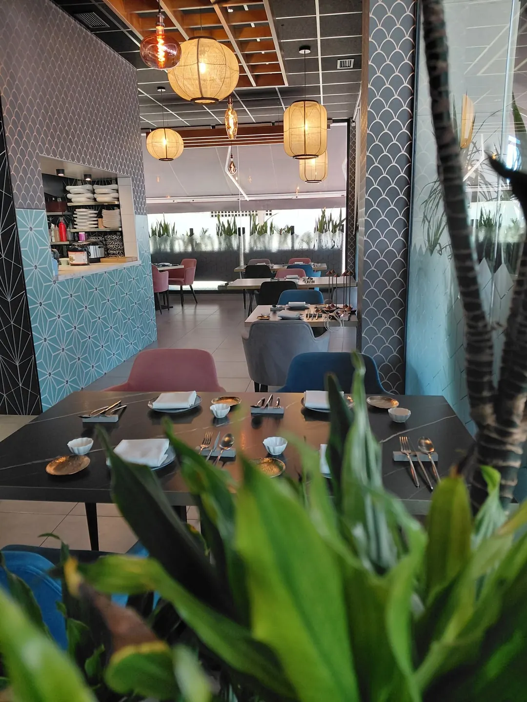 The dining room at Kuvo: paper lanterns, dark tables, velvet chairs and tiled walls, with plants in the foreground