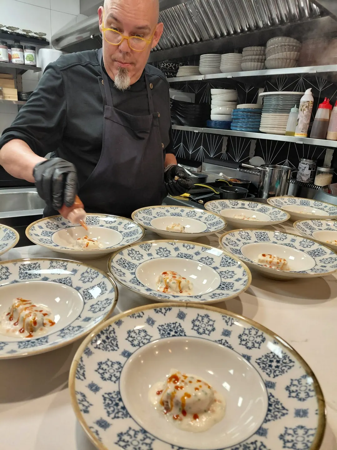Óscar saucing a line of plates on blue-and-white ceramic in the kitchen