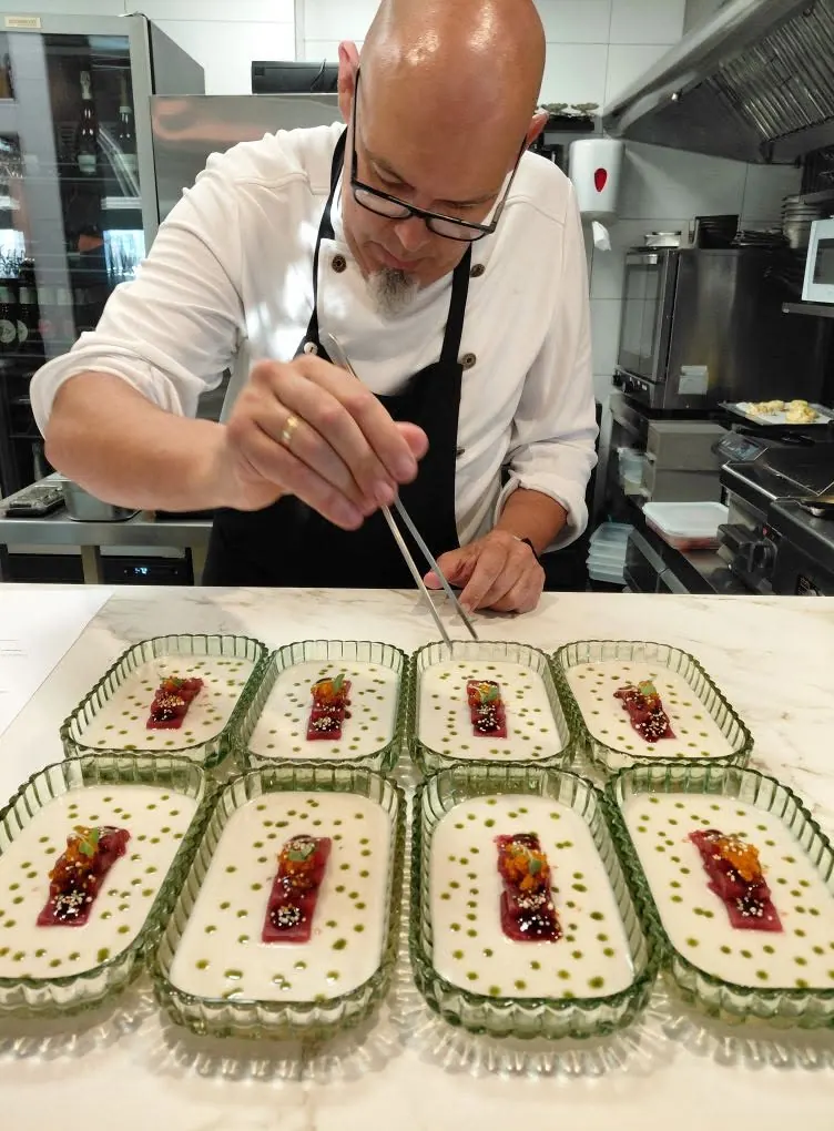Óscar placing garnish with tweezers onto a row of dishes in ribbed green glass