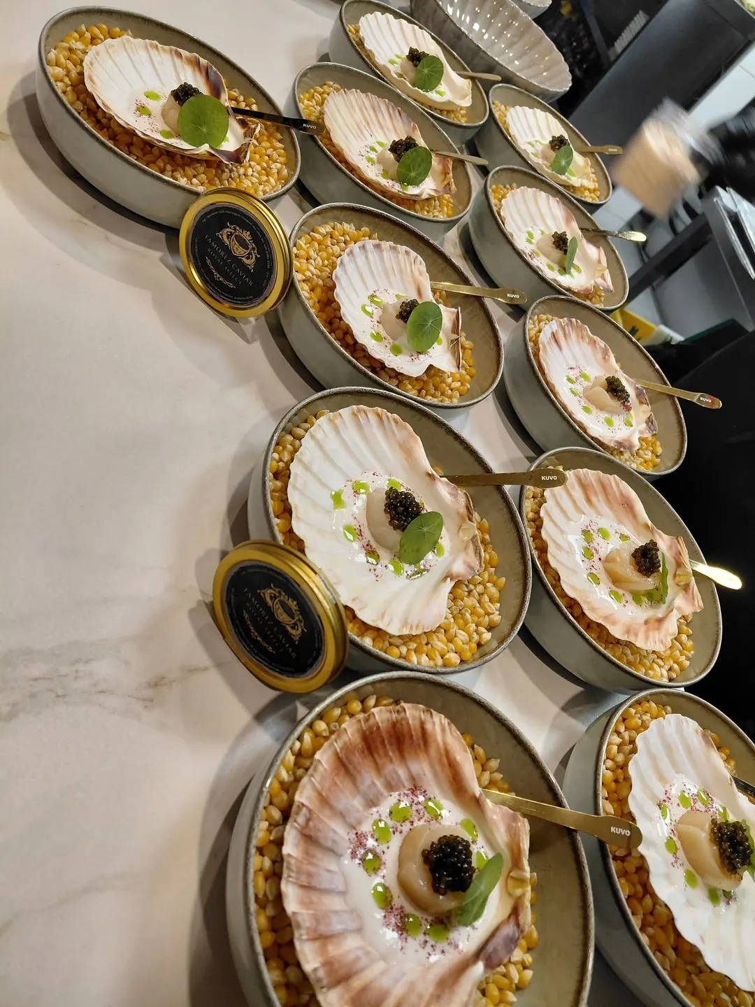 A row of scallops served in the shell, each topped with caviar, prepared in the kitchen