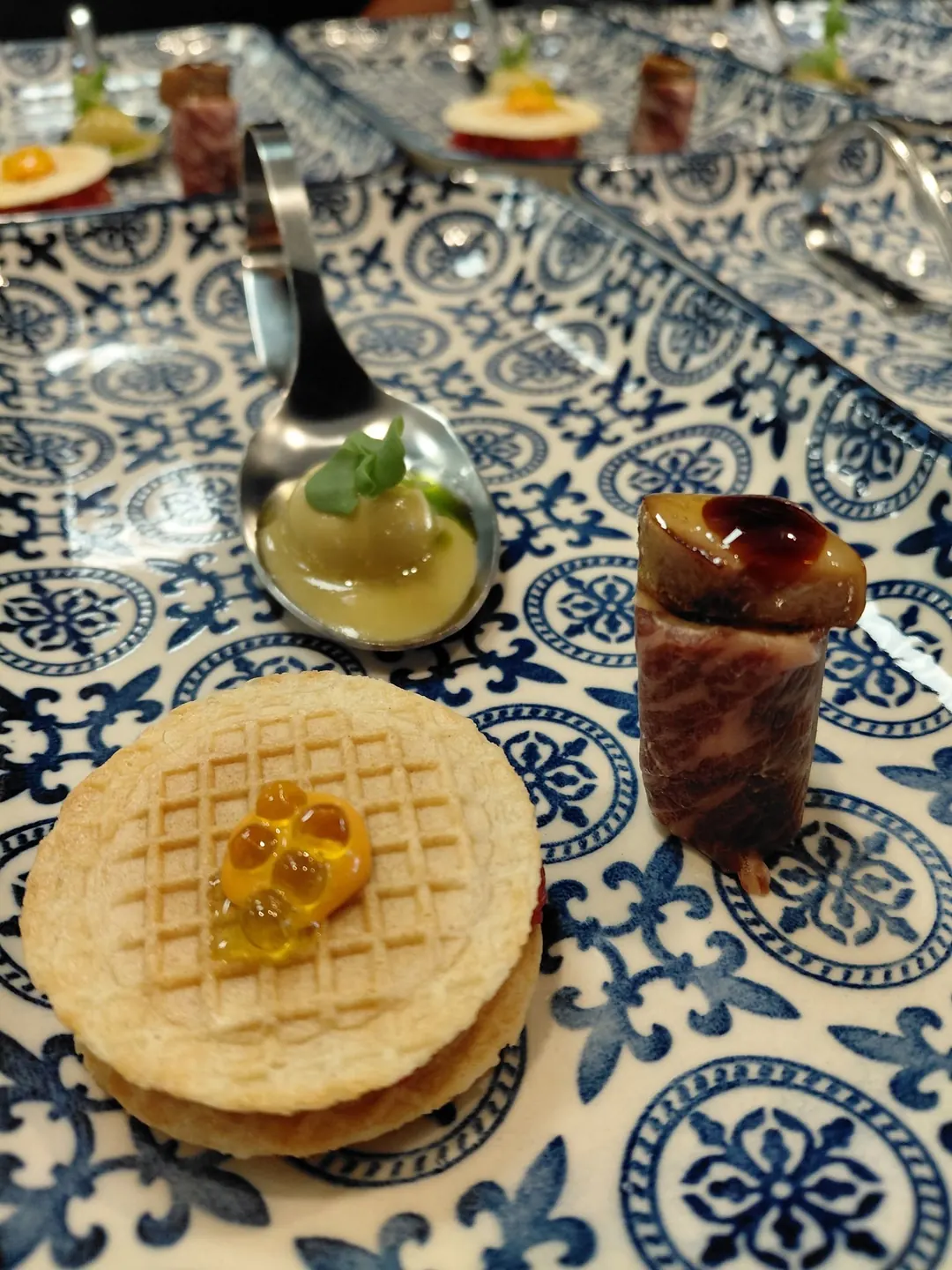 Small bites on a blue-and-white patterned plate: a spoon, a filled wafer and a rolled slice of beef