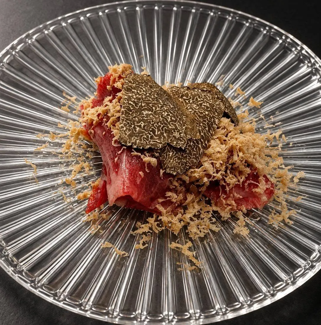 Raw beef with shaved black truffle and fine flakes on a ribbed glass plate