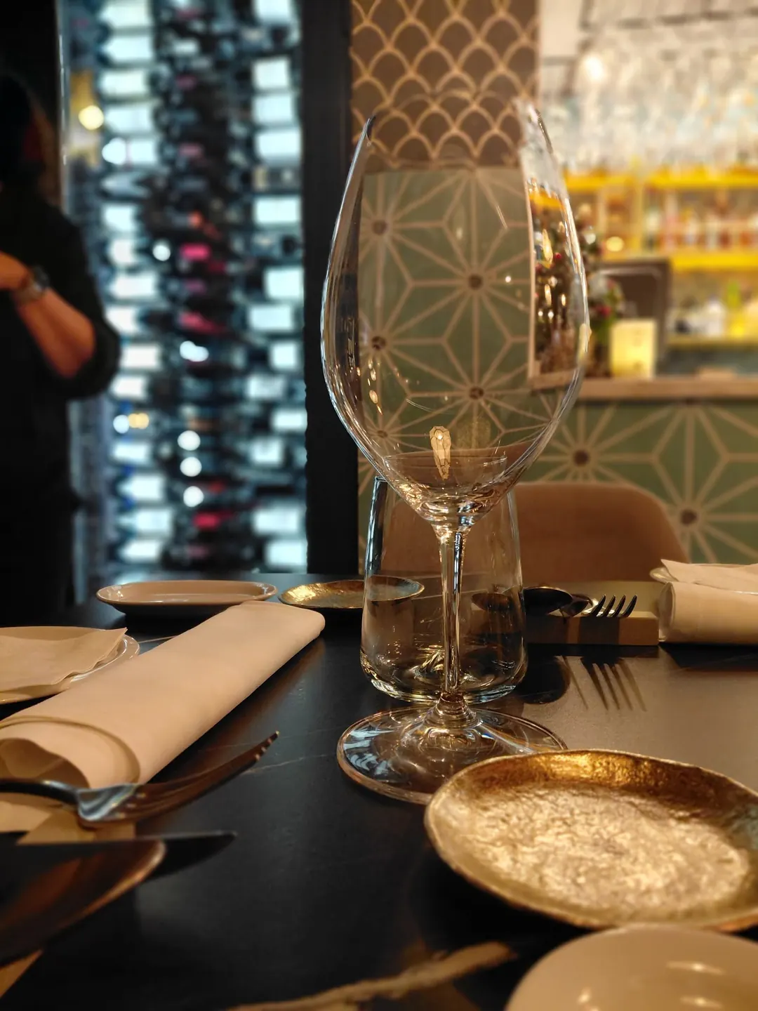 A wine glass on a laid table, with the wine wall behind